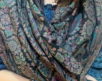 May include: A black paisley patterned shawl with gold, pink, and teal accents. The shawl is draped around a person's shoulders and neck.