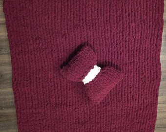 May include: A burgundy chunky knit blanket with matching burgundy arm rests and white trim. The blanket is made of thick, soft yarn and is perfect for snuggling. The arm rests are designed to be placed on the arms of a chair or sofa.