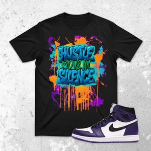 May include: Black t-shirt with the text "Hustle Move In Silence" in a graffiti style design. The shirt is paired with a high-top basketball shoe in white, black, and purple.