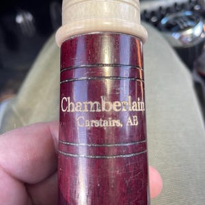 Puede incluir: Un tapón de botella de madera roja con una parte superior blanca. El tapón está grabado con el texto "Chamberlain Carstairs, AB".