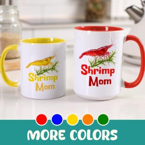 May include: Two white ceramic mugs with colorful accents. One mug has a yellow handle and interior, the other has a red handle and interior. Both mugs feature a shrimp illustration and the text "Shrimp Mom". The bottom of the image says "MORE COLORS".