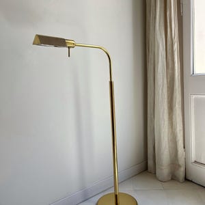 May include: A gold-coloured, mid-century modern floor lamp. The lamp has a rectangular shade with a mesh cover, a curved arm, and a round base. The lamp's height is approximately 152 cm.