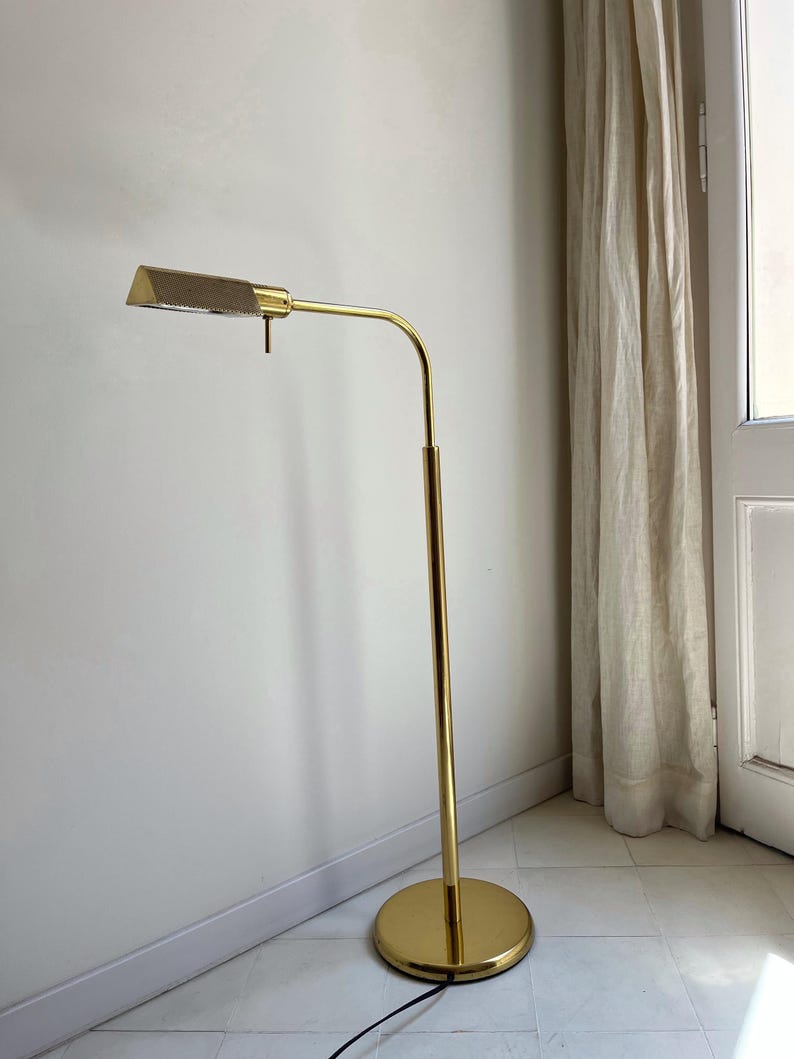 May include: A gold-coloured, mid-century modern floor lamp. The lamp has a rectangular shade with a mesh cover, a curved arm, and a round base. The lamp's height is approximately 152 cm.