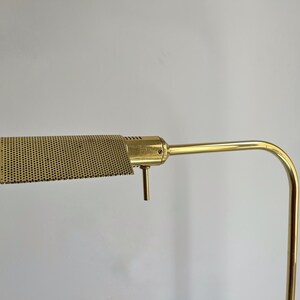 May include: A vintage brass desk lamp with a perforated shade. The lamp has a rectangular shade with a grid of small holes, a curved arm, and a vertical support. The brass finish gives the lamp a classic, retro look.