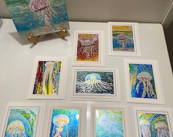 May include: A collection of art prints and greeting cards featuring jellyfish in various ocean settings. The artwork displays vibrant colors including blues, yellows, and greens, with textured paint strokes depicting underwater scenes and floating jellyfish.