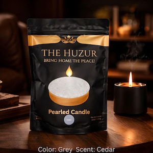 May include: A black bag with gold accents displays the text "THE HUZUR" and "BRING HOME THE PEACE!". The bag features a pearled candle graphic and the text "Pearled Candle". A lit black candle sits on a wooden table. The color is grey and the scent is cedar.