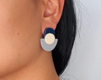 Könnte beinhalten: Ein Ohrstecker bestehend aus einem dunkelblauen, abgerundeten Oberteil, einer beigen, gesprenkelten runden Scheibe in der Mitte und einer hellgrauen, halbkreisförmigen Basis. Der geometrische Ohrring besteht aus drei geschichteten Formen.