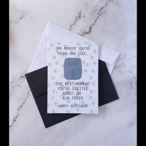 Könnte beinhalten: Eine Geburtstagskarte mit weißem Hintergrund und einem schwarzen Umschlag. Die Karte enthält den Text "ONE MOMENT YOU'RE YOUNG AND COOL, THE NEXT MOMENT YOU'RE EXCITED ABOUT AN AIR FRYER HAPPY BIRTHDAY."