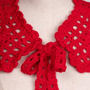 May include: A vibrant red, handmade crochet collar with a scalloped edge and a bow tie closure. The openwork design adds a delicate touch to this unique accessory. This collar is a stylish addition to any outfit.