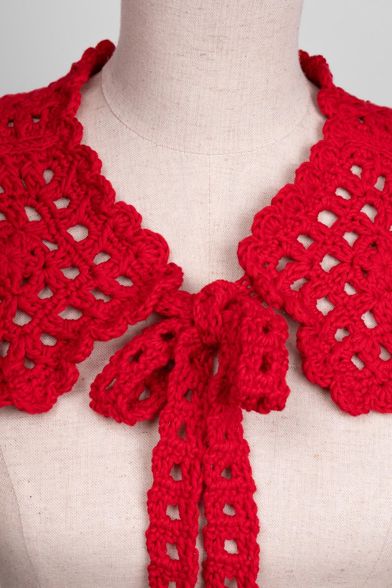 May include: A vibrant red, handmade crochet collar with a scalloped edge and a bow tie closure. The openwork design adds a delicate touch to this unique accessory. This collar is a stylish addition to any outfit.