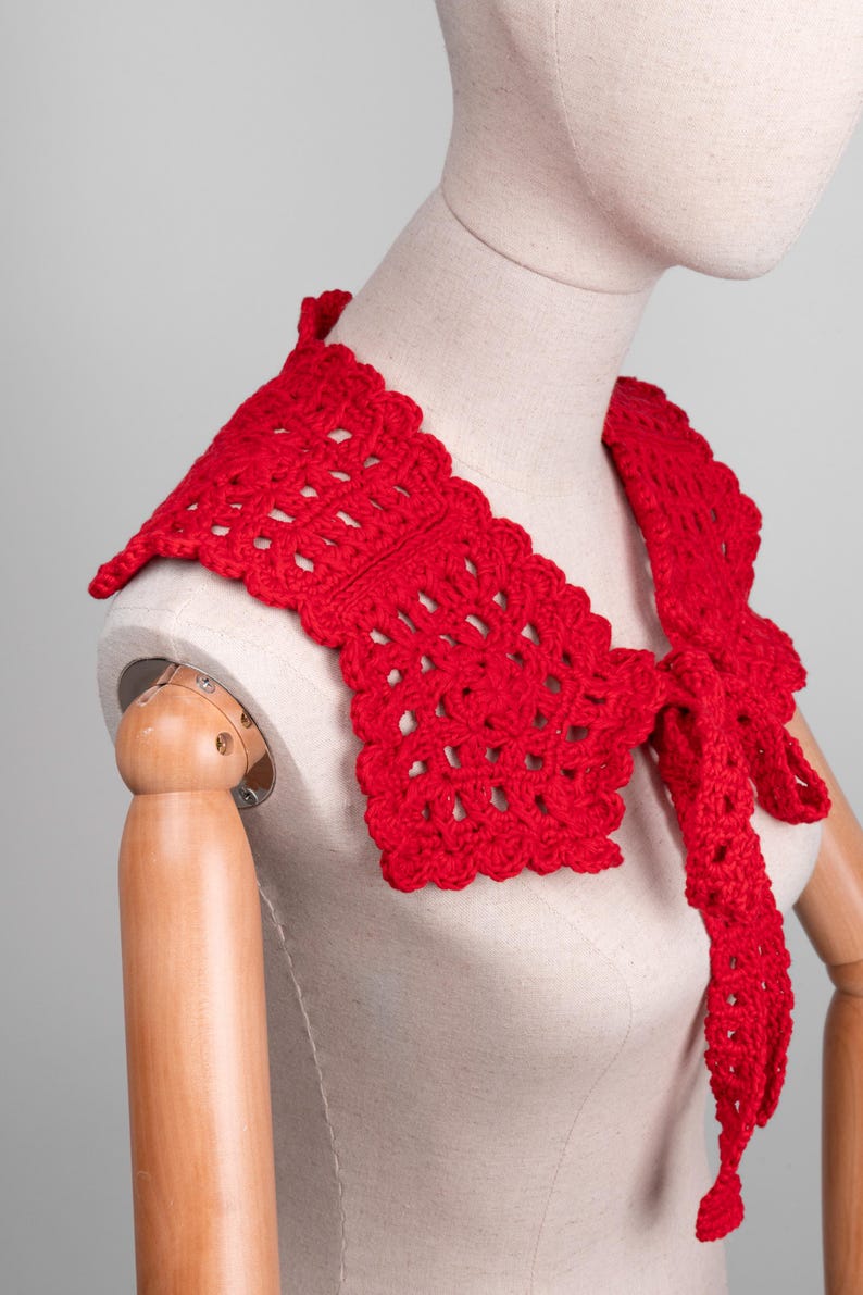 May include: A bright red, crocheted collar with a scalloped edge and a tie closure. The openwork design of the collar is visible, and it is displayed on a mannequin. The collar is a vibrant accessory.