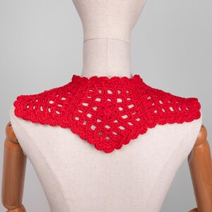 May include: A bright red, handmade crochet collar. The collar is displayed on a mannequin, showcasing its intricate openwork design and scalloped edges. The collar is a vibrant accessory.