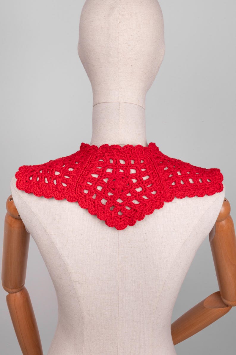 May include: A bright red, handmade crochet collar. The collar is displayed on a mannequin, showcasing its intricate openwork design and scalloped edges. The collar is a vibrant accessory.