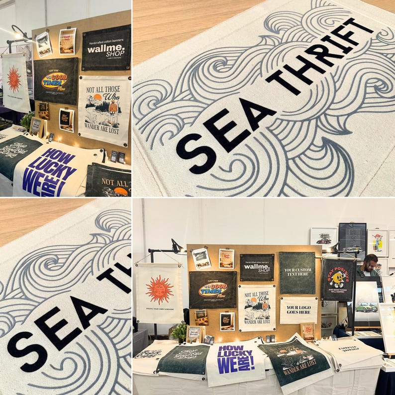 May include: A collection of rectangular fabric wall banners featuring various graphic designs and text, including the phrase SEA THRIFT in black lettering over a blue wave pattern, displayed on a wooden board and a white table surface.