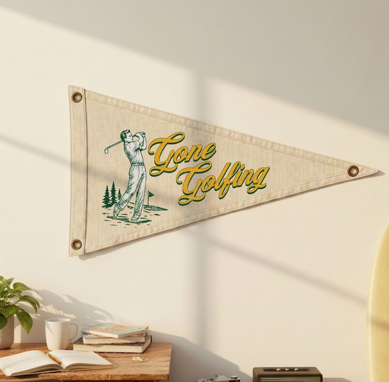 May include: A beige pennant flag with the words "Gone Golfing" in yellow script. The flag features a green and white illustration of a golfer swinging a club. The pennant has three metal grommets.