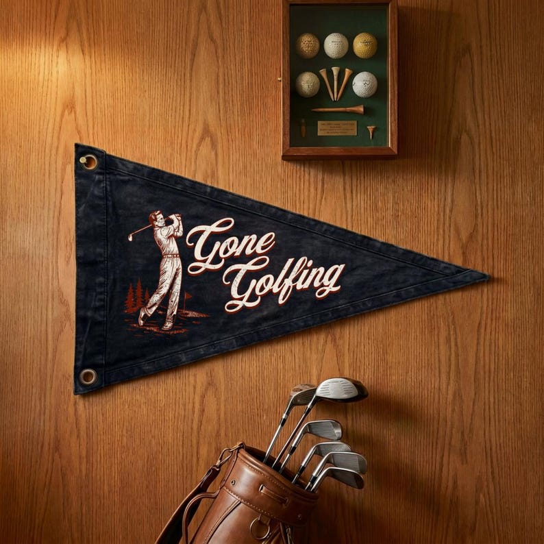 May include: A navy blue pennant with the words "Gone Golfing" in white script, featuring a golfer illustration. A brown leather golf bag with clubs is at the bottom. A framed display of golf balls and tees is at the top.