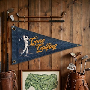 May include: A blue pennant with the words "Gone Golfing" in gold script, featuring an illustration of a golfer. The pennant hangs on a wooden wall, alongside golf clubs and a golf course map.