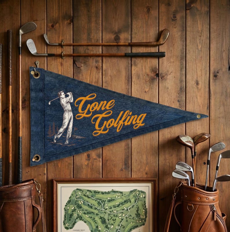 May include: A blue pennant with the words "Gone Golfing" in gold script, featuring an illustration of a golfer. The pennant hangs on a wooden wall, alongside golf clubs and a golf course map.