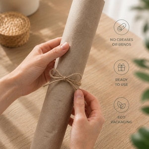 May include: A rolled-up, cylindrical package wrapped in brown paper and tied with twine. The package is held by two hands. Text on the image reads: "NO CREASES OR BENDS", "READY TO USE", and "ECO PACKAGING".