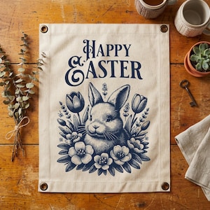 Könnte beinhalten: Ein beiges Osterbanner mit einer marineblauen Illustration eines Hasen, umgeben von Blumen und Tulpen. Die Worte "Happy Easter" sind oben aufgedruckt. Das Banner hat Metallösen in jeder Ecke.