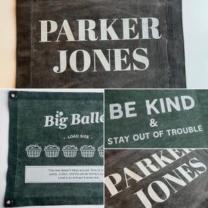May include: A dark gray and green canvas laundry bag featuring white printed text. The designs include the name PARKER JONES, the phrase BE KIND & STAY OUT OF TROUBLE, and a Big Baller graphic with laundry basket icons and descriptive text.