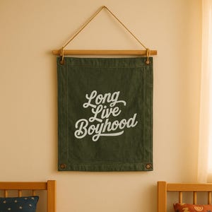 Può includere: Un arazzo da parete in tela verde con la scritta "Long Live Boyhood" in bianco. Lo striscione è sospeso a un'asta di legno con un cordino naturale. Lo striscione è rettangolare con occhielli ad ogni angolo.