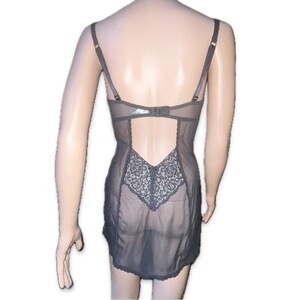 May include: A grey lingerie garment with adjustable straps and a sheer design. The back has a cut-out and a decorative lace panel. The piece is designed with a bra-like top and a skirt-like bottom.