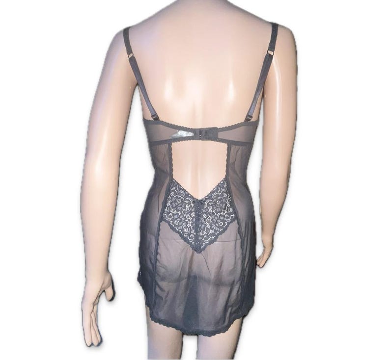 May include: A grey lingerie garment with adjustable straps and a sheer design. The back has a cut-out and a decorative lace panel. The piece is designed with a bra-like top and a skirt-like bottom.