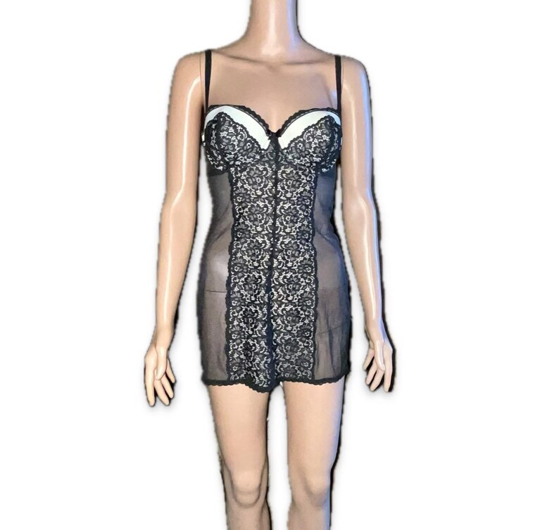 May include: Black lingerie chemise with a white bust and black lace detailing. The chemise has thin straps and a sheer skirt. The lace design is centered on the front of the chemise.