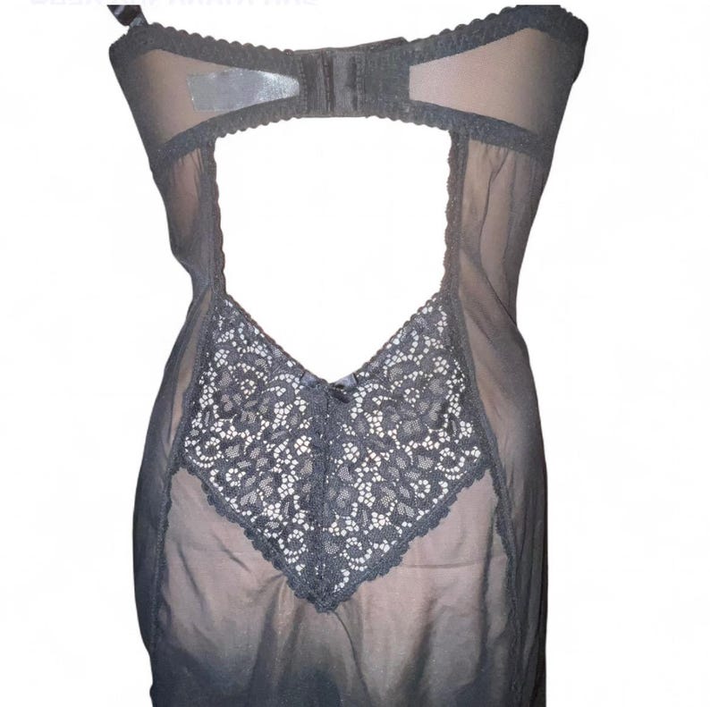 May include: A black lingerie bodysuit with a sheer design. The garment features a lace panel on the front and a bra-style top. The back is open, and the material appears to be a combination of lace and sheer fabric.
