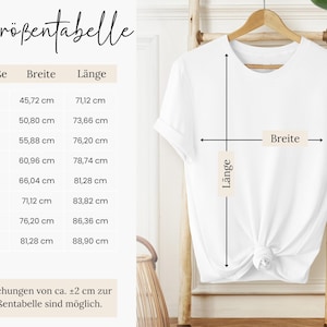 a white t-shirt hanging on a wooden hanger, with measurements and a description of the t-shirt's size and style.