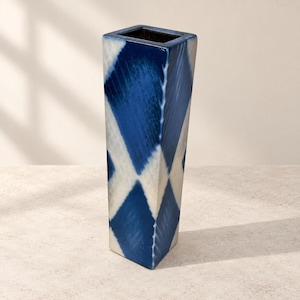 Può includere: Un vaso in ceramica alto e quadrato caratterizzato da un audace motivo a rombi dipinto a mano in blu navy intenso e bianco sporco. Il recipiente presenta una finitura liscia e lucida, un'apertura ampia e una base geometrica affusolata.