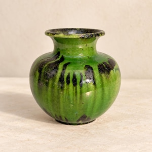 Può includere: Un piccolo vaso in ceramica bulboso caratterizzato da una vivace smaltatura verde con motivi scuri a goccia verticali. Il recipiente presenta un corpo ampio e arrotondato che si restringe verso un collo corto e svasato con finitura lucida.
