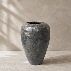 Può includere: Un grande vaso in ceramica arrotondato caratterizzato da una smaltatura grigio scuro e antracite maculata con sottili riflessi bronzo metallizzato. La superficie presenta una finitura lucida e testurizzata con motivi a goccia e un bordo circolare.