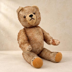 Könnte beinhalten: Ein Teddybär im Vintage-Stil mit hellbraunem, zotteligem Fell und einer helleren beigen Schnauze. Der Bär hat eine schwarz gestickte Nase und einen Mund, dunkle Augen sowie strukturierten, goldbraunen Cordstoff an den Fußsohlen und einer Pfote.