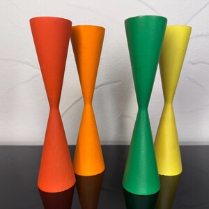 Può includere: Quattro portacandele alti e sottili con una distinta forma a clessidra. Ogni portacandele presenta una finitura opaca a tinta unita in un colore vivace diverso: uno rosso, uno arancione, uno verde e uno giallo. Hanno base e cima larghe.