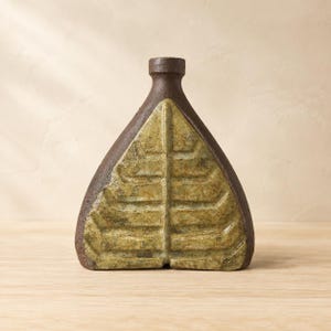 Peut inclure: Un vase en céramique triangulaire avec un col et une base en terre cuite brun foncé texturée. La face avant présente un motif en relief en forme de feuille avec une glaçure vert olive mouchetée, contrastant avec le corps sombre et rugueux.