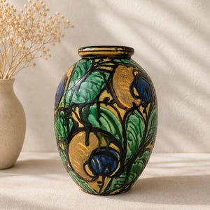 Può includere: Un vaso in ceramica ovale con un design dipinto a mano di foglie verdi, motivi circolari giallo oro e accenti blu intenso. La superficie ha una finitura lucida con contorni scuri in rilievo che definiscono i motivi botanici presenti.