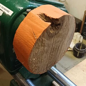 Może przedstawiać: Zbliżenie na tokarkę do drewna z zamontowanym na niej kawałkiem drewna. Drewno jest pomalowane na pomarańczowo i ma sęk. Tokarka jest zielona i ma metalowy uchwyt.