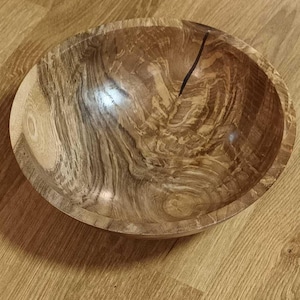 Może przedstawiać: Duża drewniana miska z naturalnym, brązowym wykończeniem. Miska ma unikalny, wirujący wz&oacute;r słoj&oacute;w i ciemnobrązową linię biegnącą w d&oacute;ł środka.