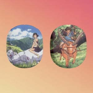 May include: Two round, colorful, ceramic plates with images of characters from the animated film Princess Mononoke. The first plate features a young woman riding a white wolf, while the second plate shows a man riding a deer-like creature with large antlers.
