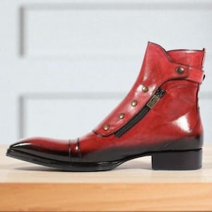 May include: A red leather boot with a pointed toe and a black sole. The boot features a side zipper, decorative buttons, and a small buckle detail. The leather has a glossy finish and a gradient effect, transitioning from red to black.