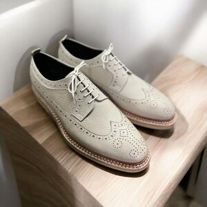 May include: A pair of off-white leather brogue shoes with white laces. The shoes have a wingtip design and a textured leather upper.