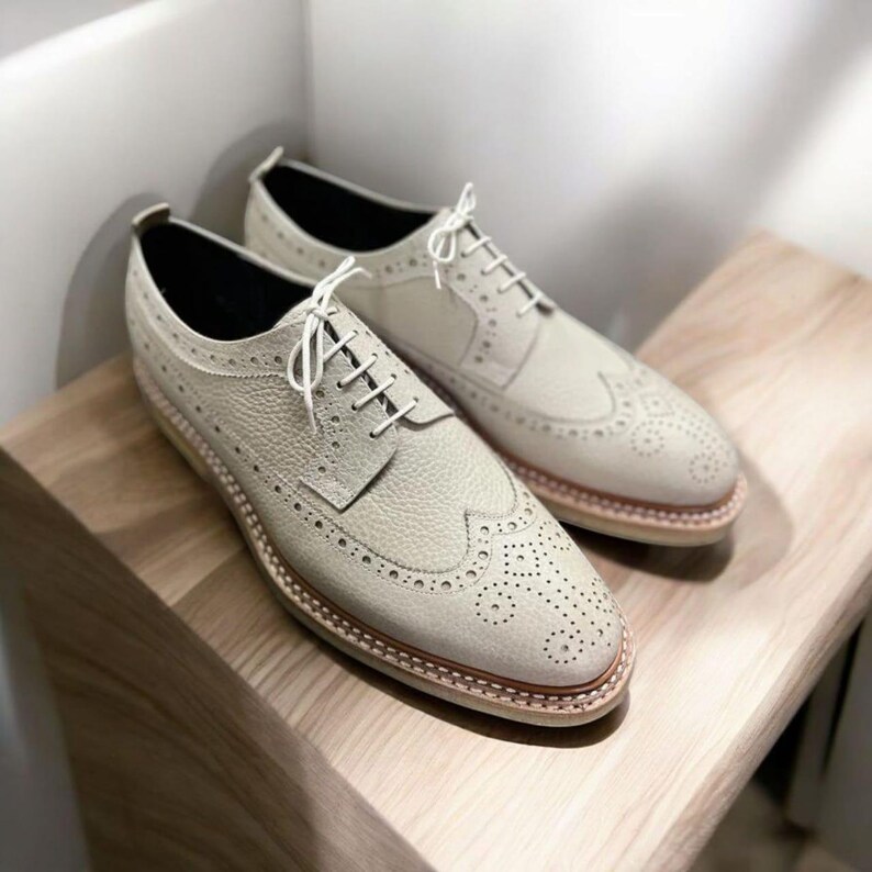 May include: A pair of off-white leather brogue shoes with white laces. The shoes have a wingtip design and a textured leather upper.