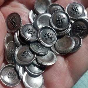 May include: A collection of small, round, dark silver discs with raised edges. Each disc is stamped with the text 18, FINE SILVER, and 999. The metal has a weathered, oxidized finish with visible dark patina in the recessed areas and lighter highlights on the raised lettering and rims.