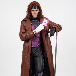 May include: A costume featuring a long brown leather trench coat, a purple and black bodysuit, black boots, and purple leg armor. The outfit includes a black headpiece, gold wrist cuffs, white gloves, and a silver staff, with a glowing playing card.