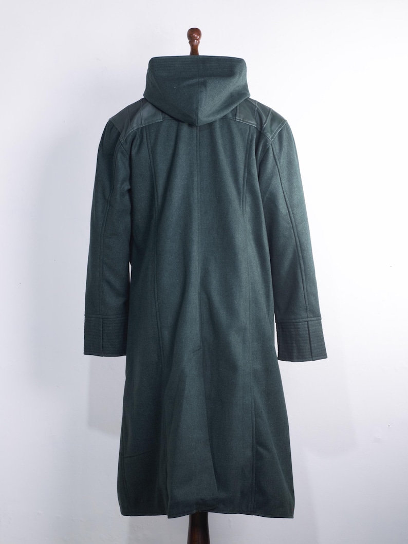 May include: A dark green hooded coat with a long, tailored design. The coat features a hood, structured shoulders, and detailed cuffs. The coat is displayed on a wooden hanger against a white background.