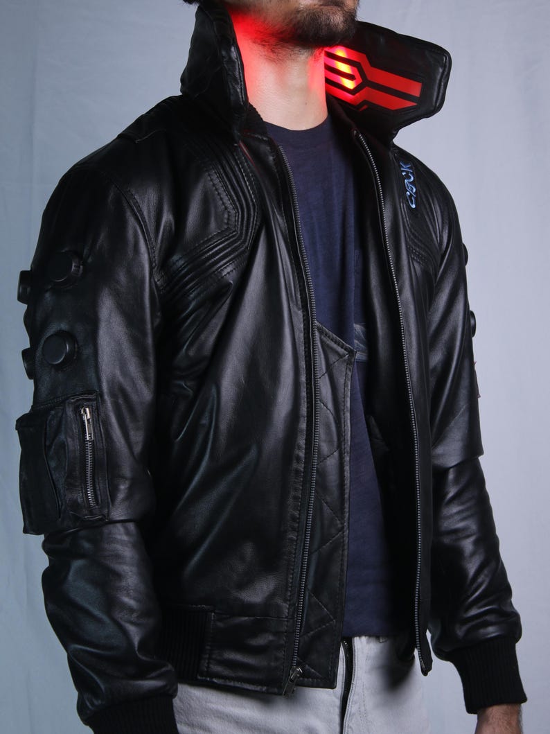 May include: A black leather jacket featuring a high collar with a glowing red light panel, a zippered utility pocket on the sleeve, and circular black accents. The jacket has a quilted front panel, ribbed cuffs, and a blue graphic detail on the shoulder.