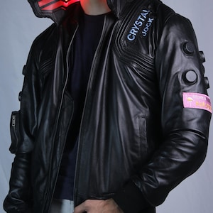 May include: A black leather jacket featuring a high collar with an illuminated red light panel, a front zipper, and black circular accents on the sleeves. A patch on the chest reads CRYSTAL JOCK, and a pink rectangular patch on the arm displays a flamingo.