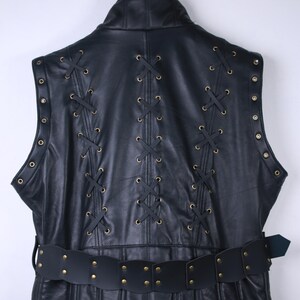 May include: Black leather vest with decorative lacing and a matching belt. The vest features brass-colored grommets and a high collar. The belt has brass-colored rivets. The vest is hanging on a metal hanger.